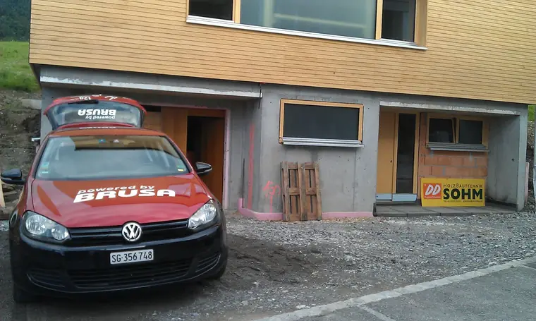 BRUSA e-Golf in front of a building shell with timber facade and a Sohm Holzbautechnik site sign