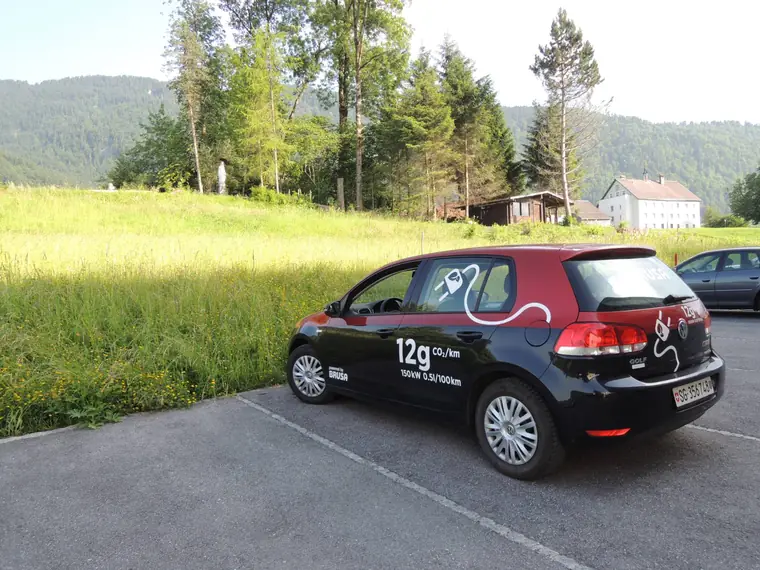 Electric VW Golf with BRUSA branding in front of a mountain meadow