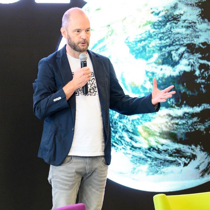 Christoph J. Sorg speaking with a microphone on stage, the Earth seen from space behind him